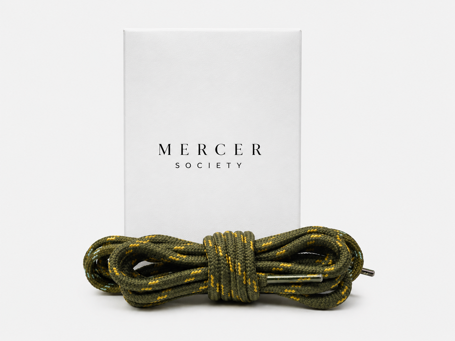 Army green Mercer Society laces for sneakers, showing close-up of twisted shoelaces on a pair of casual shoes.