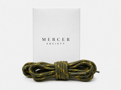 Army green Mercer Society laces for sneakers, showing close-up of twisted shoelaces on a pair of casual shoes.